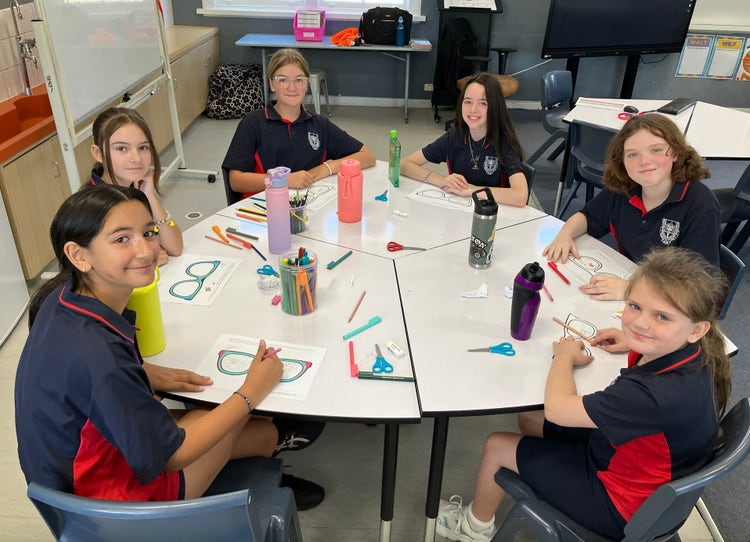 Six female students sitting at a table, doing art.