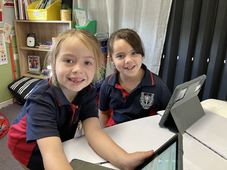 Two female students smiling and looking at the camera and holding tablets.